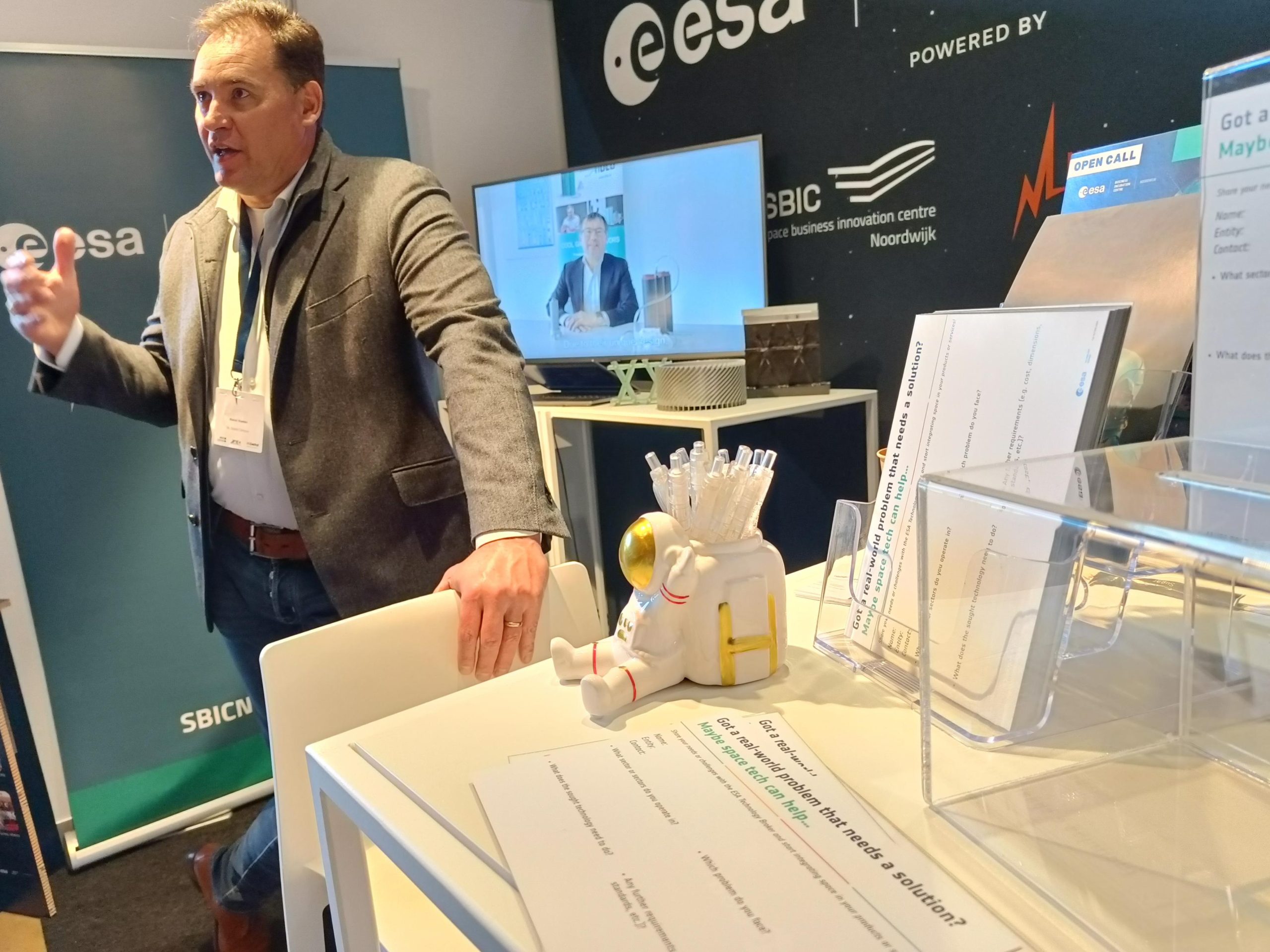 space tech broker at an exhibition booth with media screen and small astronaut pen holder in the foreground