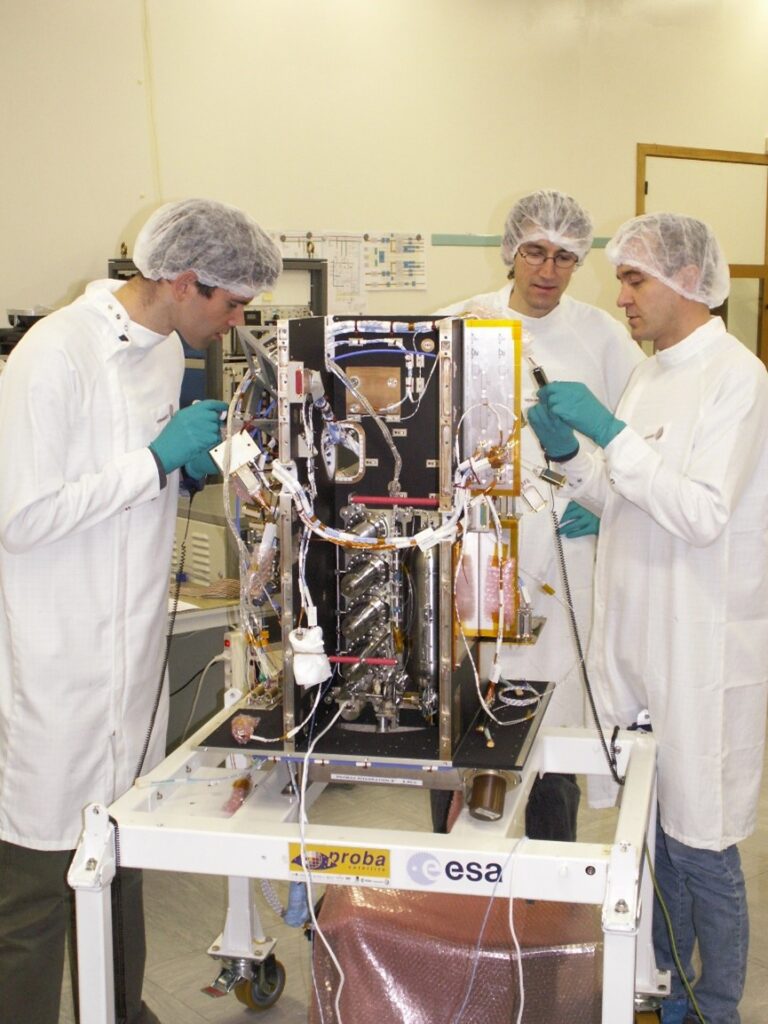 three aerospace engineers preparing satellite hardware